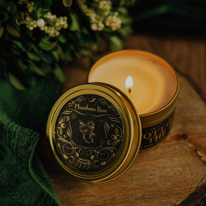Lit Cottage by the Sea 3.3 oz gold tin soy candle with lid propped on side of tin showing detail of black and gold foil label.
