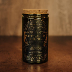 Front shot of Cottage by the Sea 15 oz soy candle with a vintage green glass jar, cork top, and black and gold foil label with vintage illustrations.