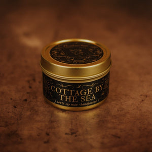 Front shot of Cottage by the Sea 3.3 oz soy candle in a gold tin with top and black and gold foil labels with vintage illustrations on the front and lid.