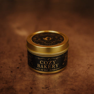 Front shot of Cozy Bakery 3.3 oz soy candle in a gold tin with top and black and gold foil labels with vintage illustrations on the front and lid.