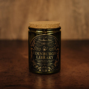 Front shot of Edinburgh Library 11 oz soy candle with a vintage green glass jar, cork top, and black and gold foil label with vintage illustrations.