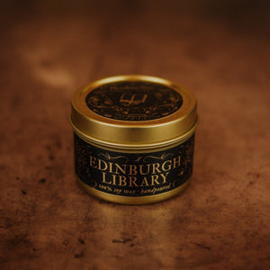 Front shot of Edinburgh Library 3.3 oz soy candle in a gold tin with top and black and gold foil labels with vintage illustrations on the front and lid.