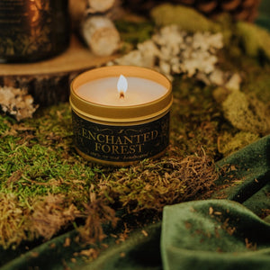 Lit Enchanted Forest 3.3 oz gold tin soy candle placed on moss and green velvet.