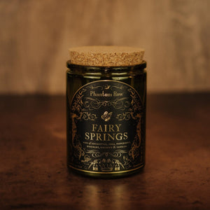 Front shot of Fairy Springs 11 oz soy candle with a vintage green glass jar, cork top, and black and gold foil label with vintage illustrations.