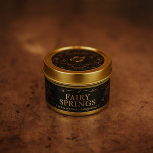 Front shot of Fairy Springs 3.3 oz soy candle in a gold tin with top and black and gold foil labels with vintage illustrations on the front and lid.
