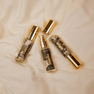 Phantom Row mini-sized Ritual Mists in 0.3 oz glass atomizer vials with gold lids arranged on cream fabric. Root, Vigor, and Soothe labels show black and white vintage illustrations with the names in gold foil.
