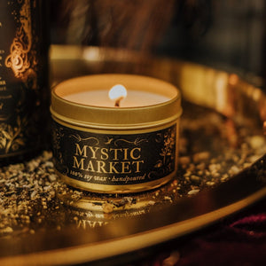 Close up of lit Mystic Market gold soy candle tin sitting on a reflective gold platter.