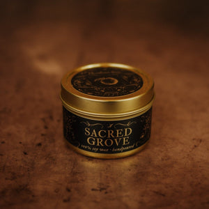 Front shot of Sacred Grove 3.3 oz soy candle in a gold tin with top and black and gold foil labels with vintage illustrations on the front and lid.