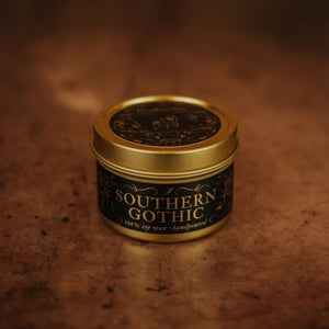 Front shot of Southern Gothic 3.3 oz soy candle in a gold tin with top and black and gold foil labels with vintage illustrations on the front and lid.