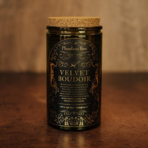 Front shot of Velvet Boudoir 15 oz soy candle with a vintage green glass jar, cork top, and black and gold foil label with vintage illustrations.