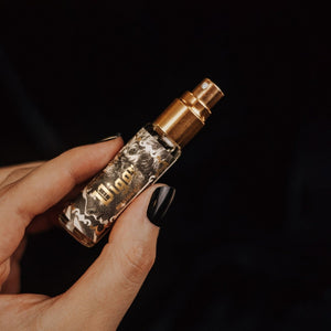 Hand holding mini-sized Vigor Ritual Mist with gold atomizer and black-and-white label with a vintage illustration and the name in gold foil.