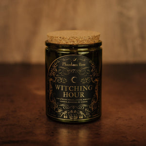 Front shot of Witching Hour 11 oz soy candle with a vintage green glass jar, cork top, and black and gold foil label with vintage illustrations.